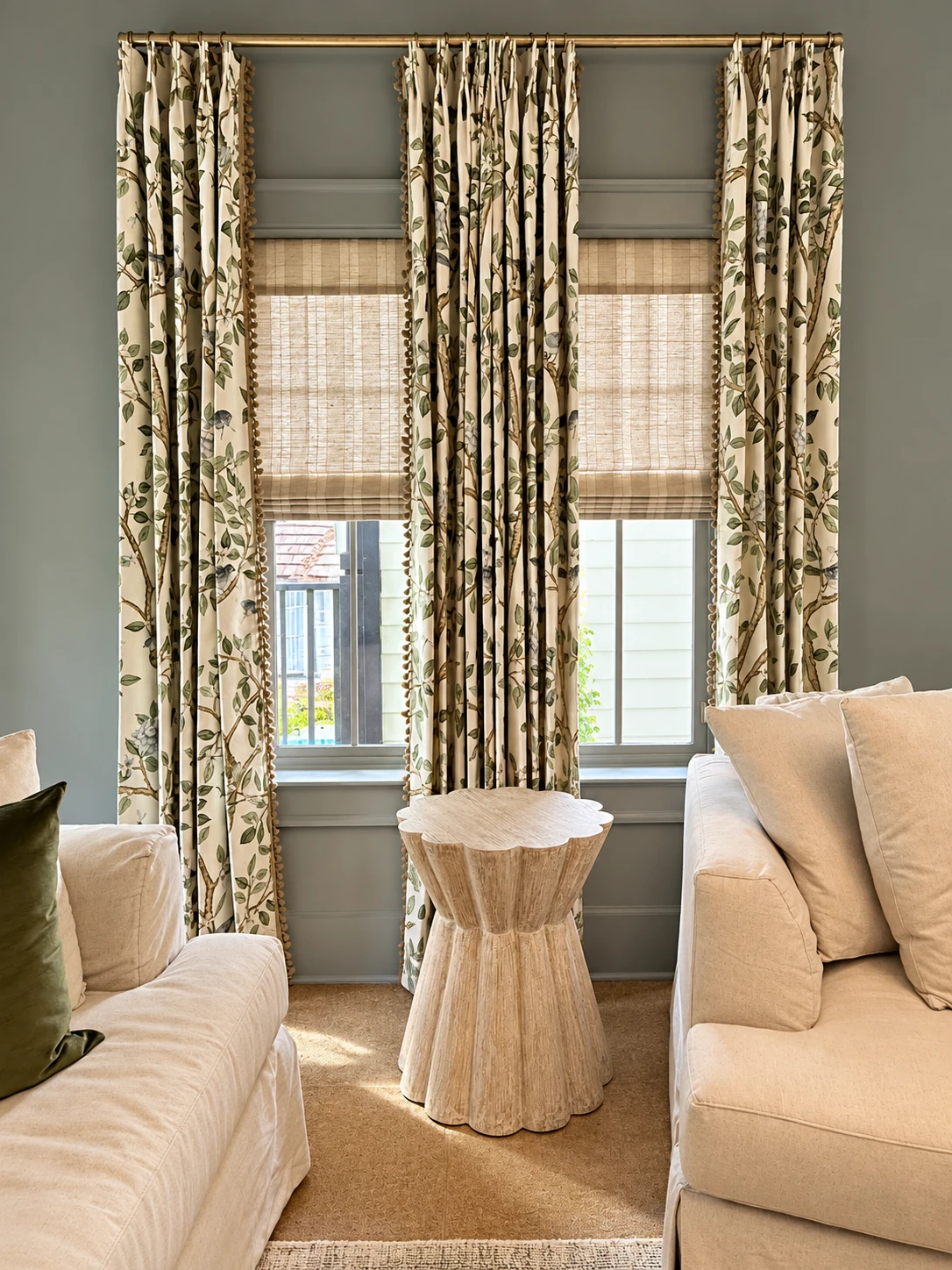 Botanical-print drapery on a brass rod layered over woven shades in a furnished living room
