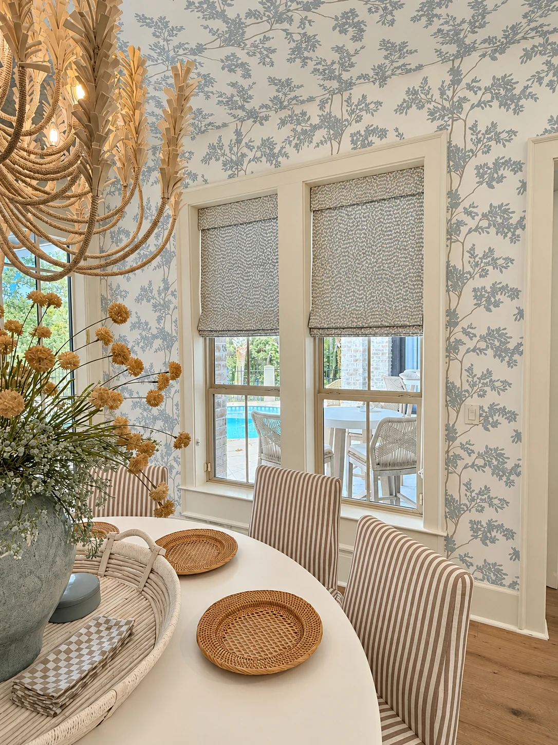 Two patterned Roman shades fitted in adjacent dining-room windows above upholstered chairs