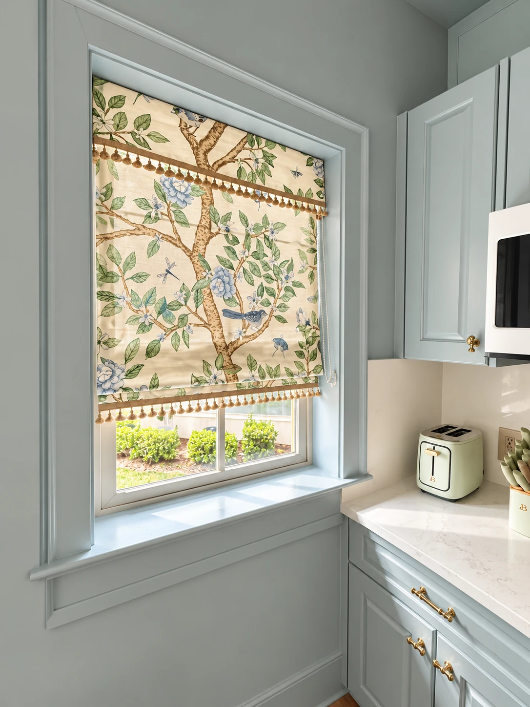 Botanical and bird-print Roman shade with tassel trim over a kitchen window