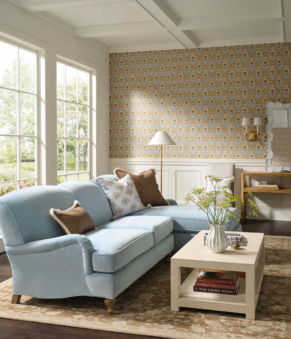 Serena & Lily Palmetto wallpaper installed behind a pale blue sectional in a sunlit living room.