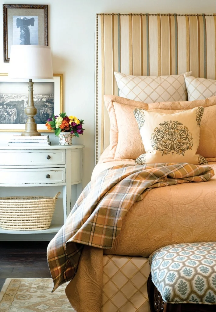 Styled bedroom interior featuring Stroheim Color Gallery upholstery fabrics: a striped upholstered headboard, patterned pillows, quilted bedding, and a plaid throw in warm neutral tones.